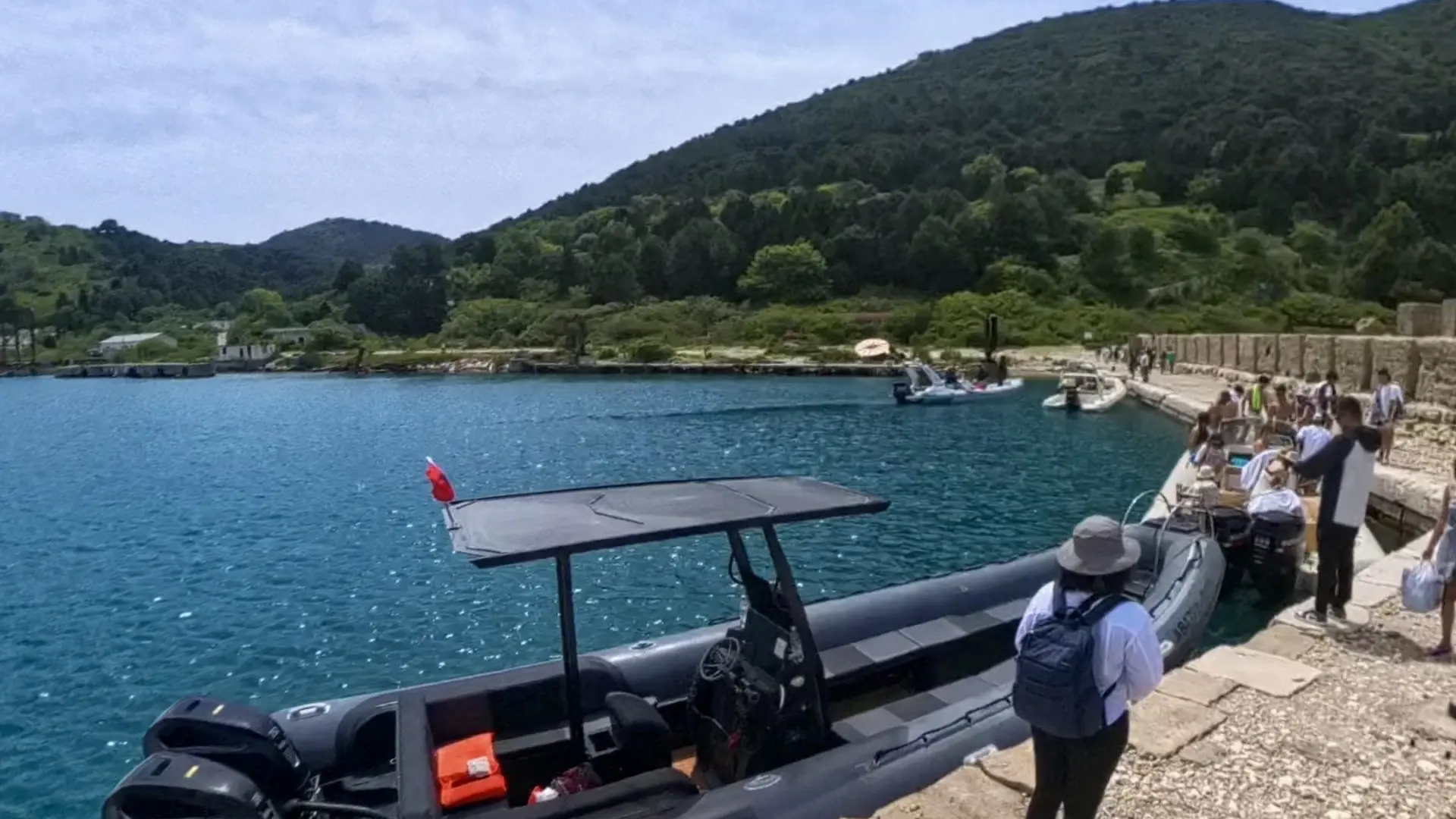 A black rigid inflatable speedboat moored at a stone pier on Sazan while passengers walk ashore